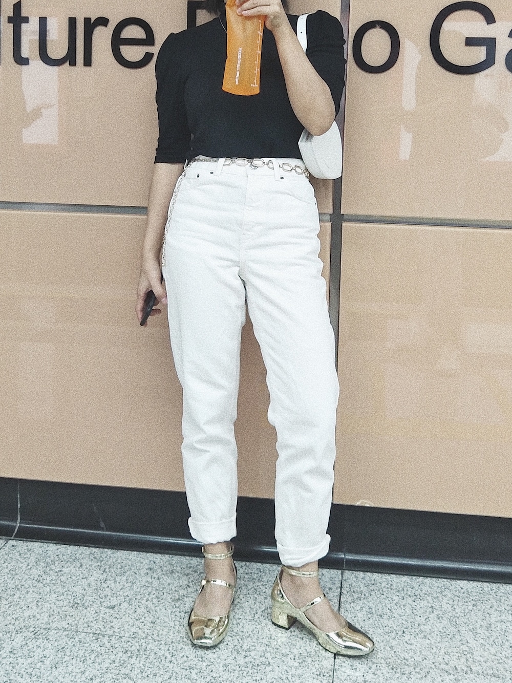 ホワイト系のデニムパンツ、ブラック系のニット/セーター、ゴールド系のベルトを着用したレディースの冬コーディネートの1枚目の写真