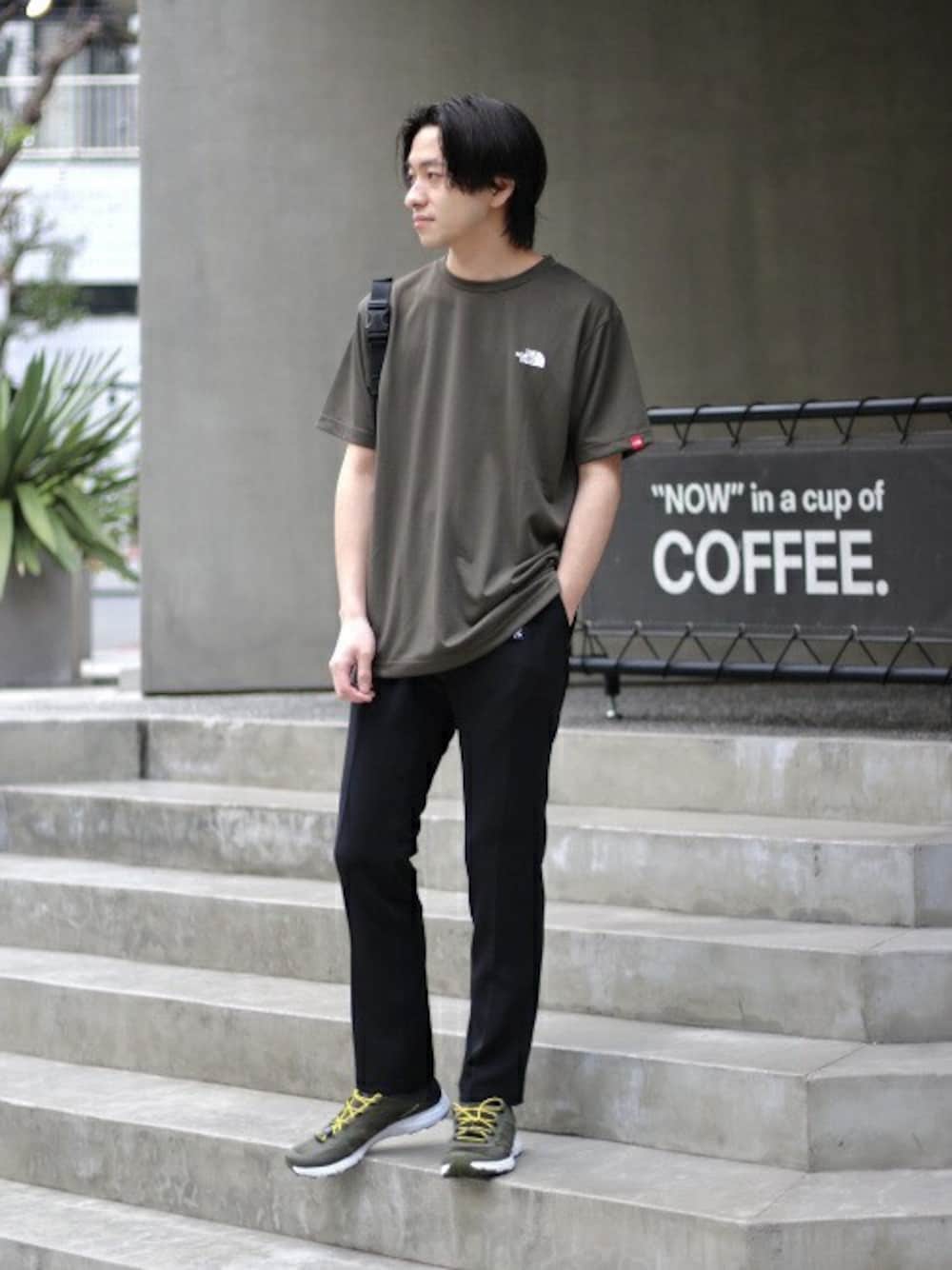 グリーン系のTシャツ/カットソー、ブラック系のスラックス、グリーン系のスニーカーを着用したメンズの春コーディネートの1枚目の写真