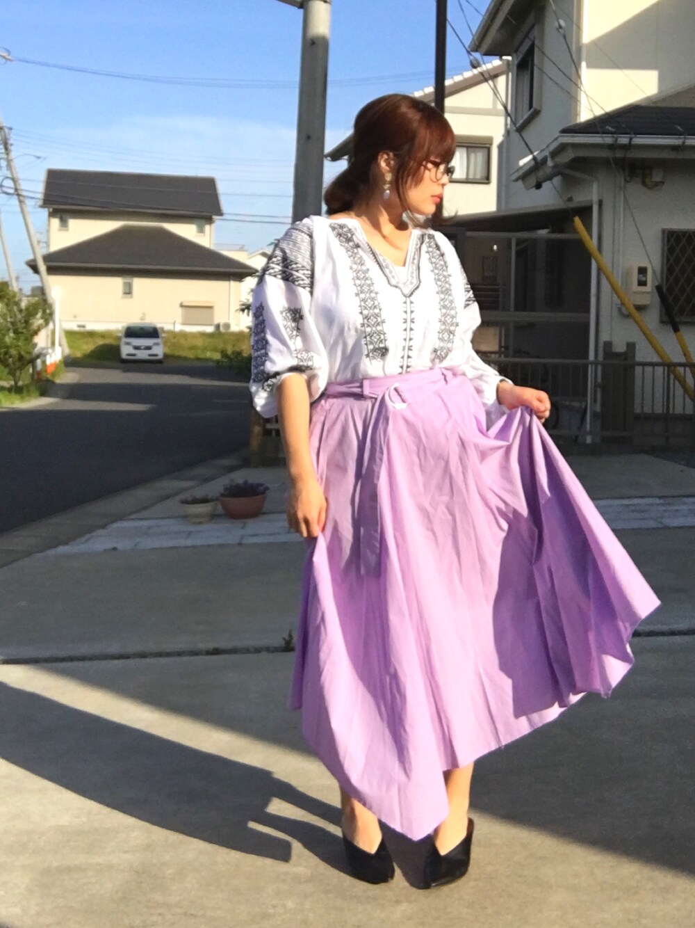ブラック系のパンプス、ホワイト系のトップス、パープル系のスカートを着用したレディースの春コーディネートの1枚目の写真