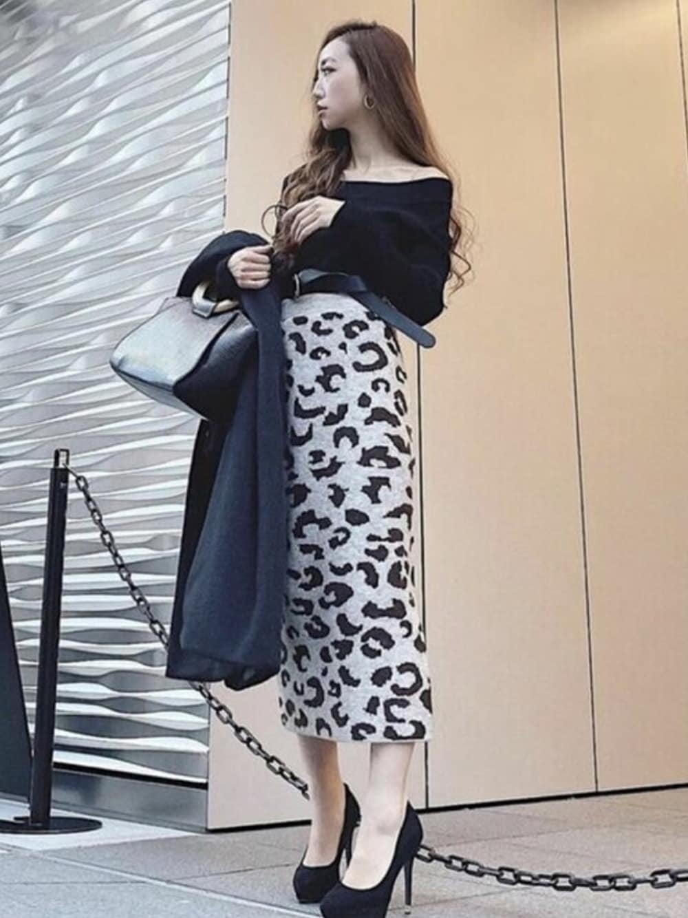 ブラック系のニット/セーター、ブラウン系のスカート、ブラック系のハンドバッグを着用したレディースの冬コーディネートの1枚目の写真