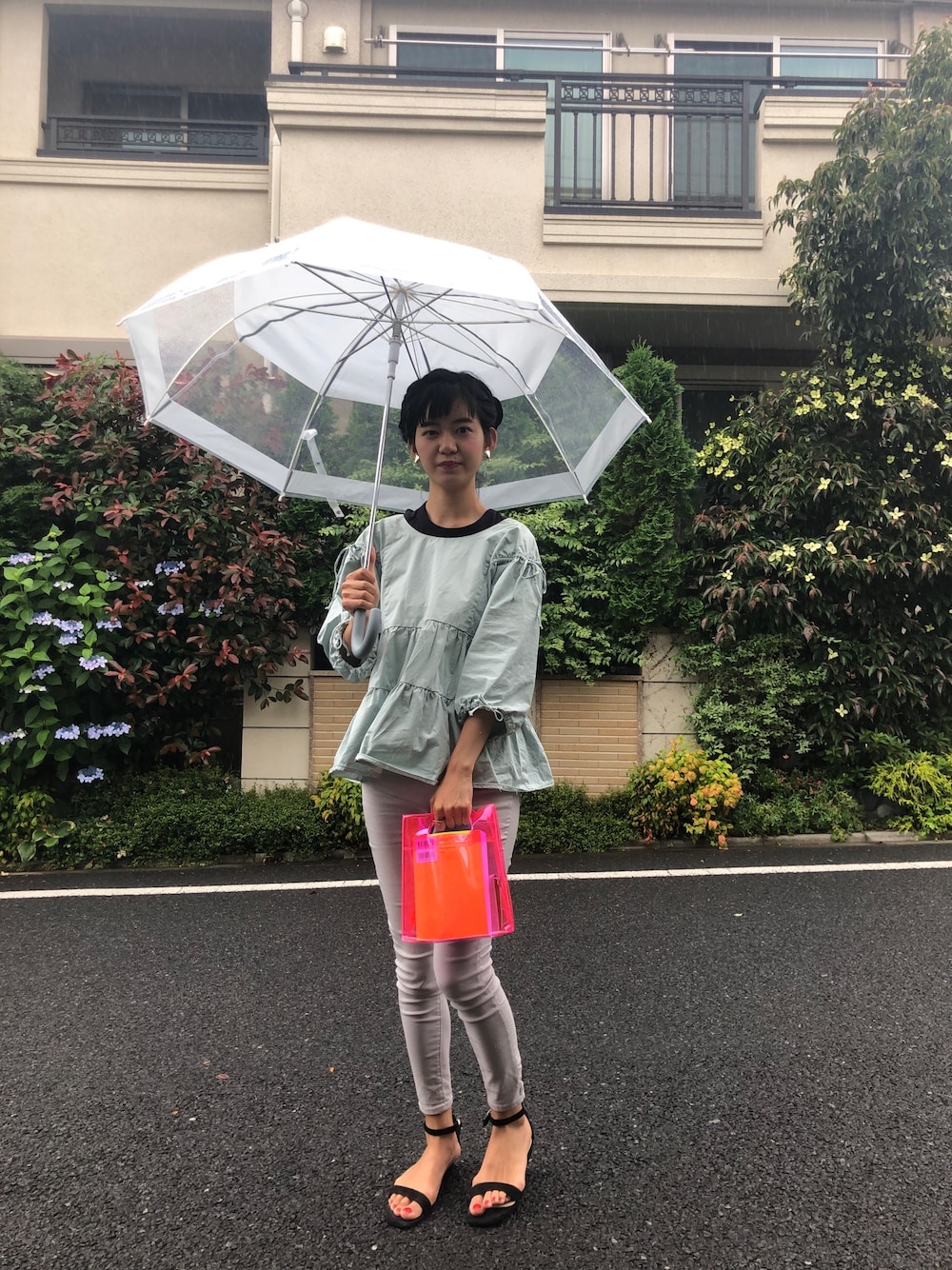 グリーン系のシャツ/ブラウス、レッド系のクラッチバッグ、グレー系のパンツを着用したレディースの夏コーディネートの1枚目の写真