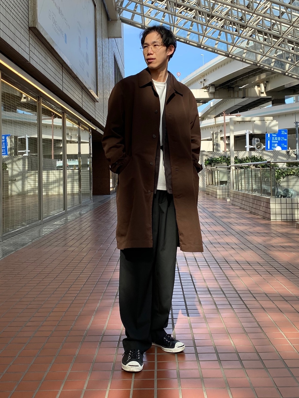 ブラウン系のステンカラーコート、ブラック系のスラックスを着用したメンズの春コーディネートの1枚目の写真