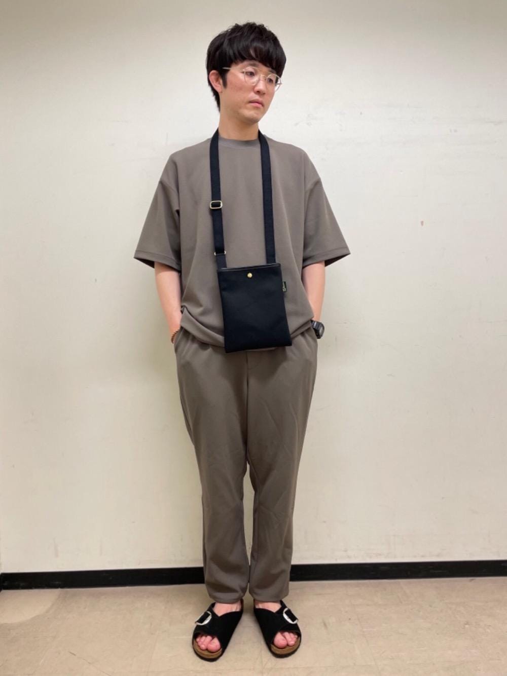 ブラック系のショルダーバッグ、ブラック系のサンダル、ベージュ系のTシャツ/カットソーを着用したメンズの春コーディネートの1枚目の写真