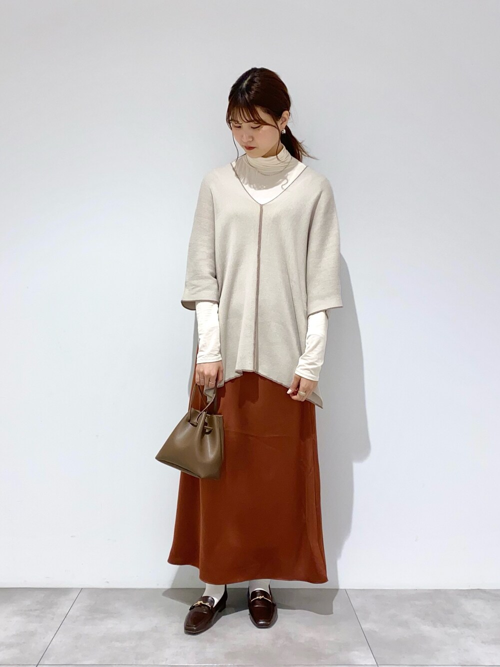 ベージュ系のニット/セーター、ホワイト系のTシャツ/カットソー、ブラウン系のスカートを着用したレディースの春コーディネートの1枚目の写真