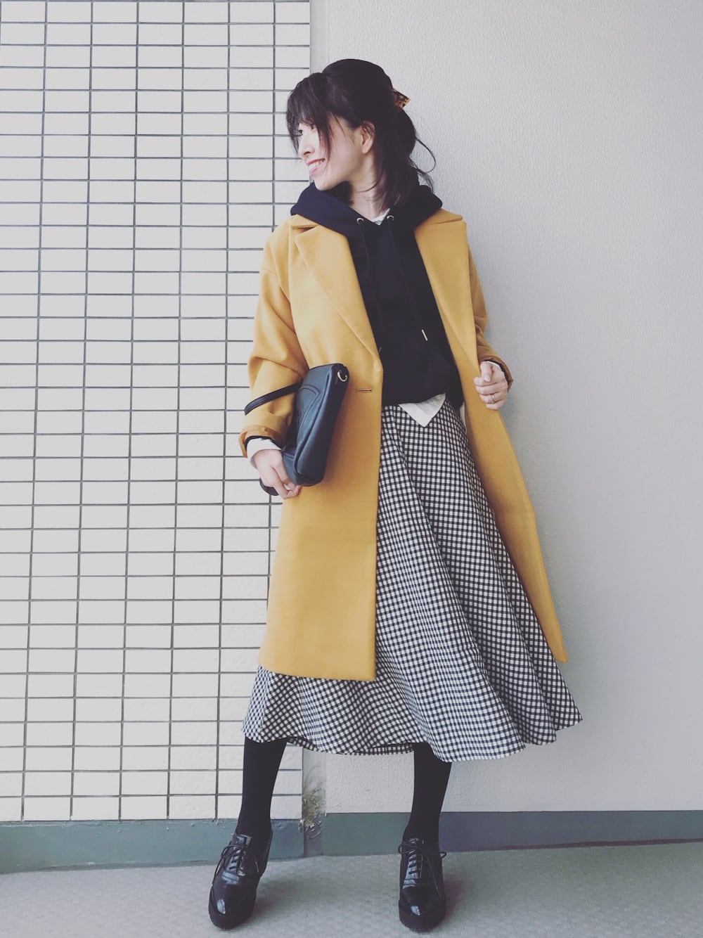 イエロー系のチェスターコート、ホワイト系のシャツ/ブラウス、ブラック系のスカートを着用したレディースの冬コーディネートの1枚目の写真