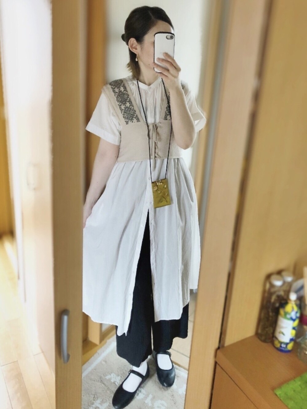 ホワイト系のシャツワンピース、ベージュ系のベスト、ブラック系のその他パンツを着用したレディースの秋コーディネートの1枚目の写真