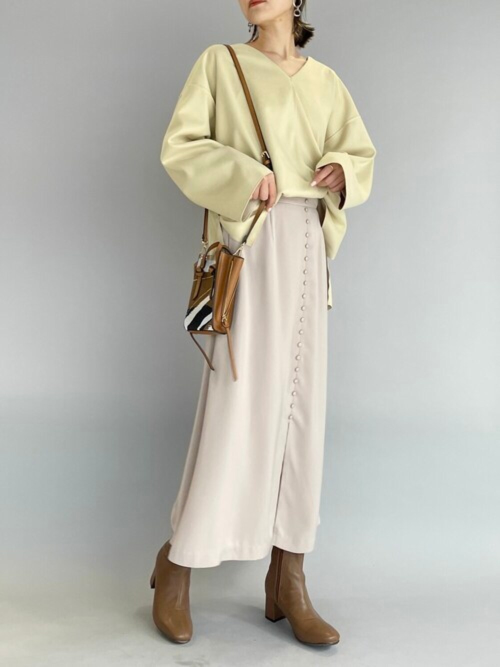 イエロー系のTシャツ/カットソー、ベージュ系のスカート、ブラウン系のブーツを着用したレディースの秋コーディネートの1枚目の写真