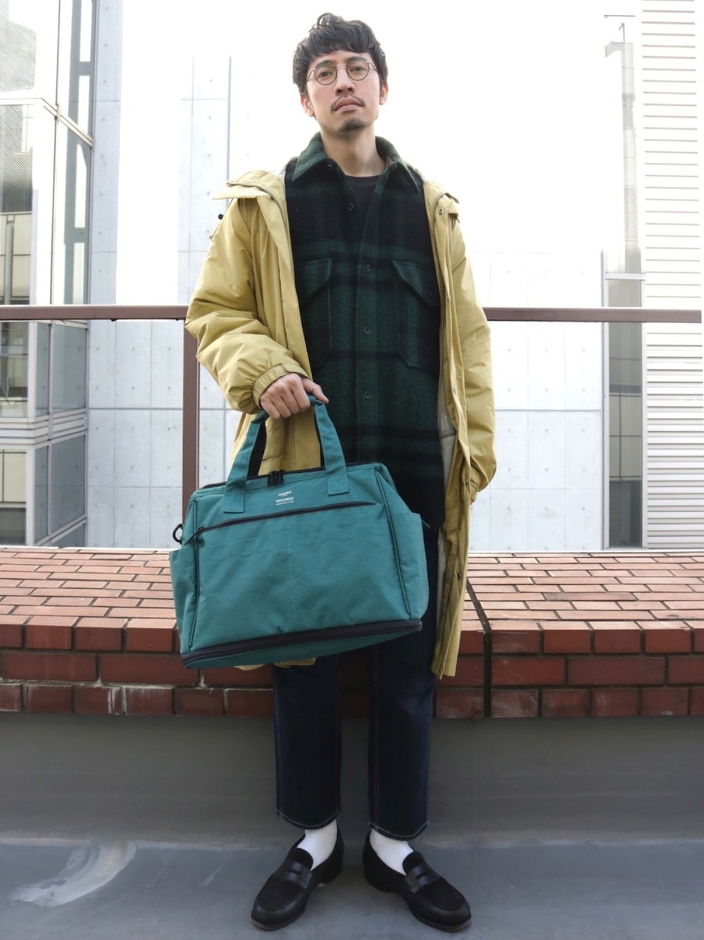 グリーン系のショルダーバッグ、ブラック系のドレスシューズ、ブルー系のデニムパンツを着用したメンズの冬コーディネートの1枚目の写真