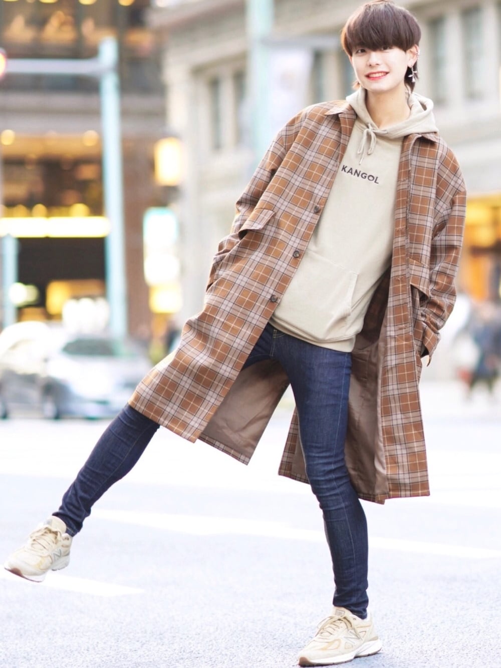 ベージュ系のステンカラーコート、ベージュ系のパーカー、ブルー系のデニムパンツを着用したメンズの春コーディネートの1枚目の写真