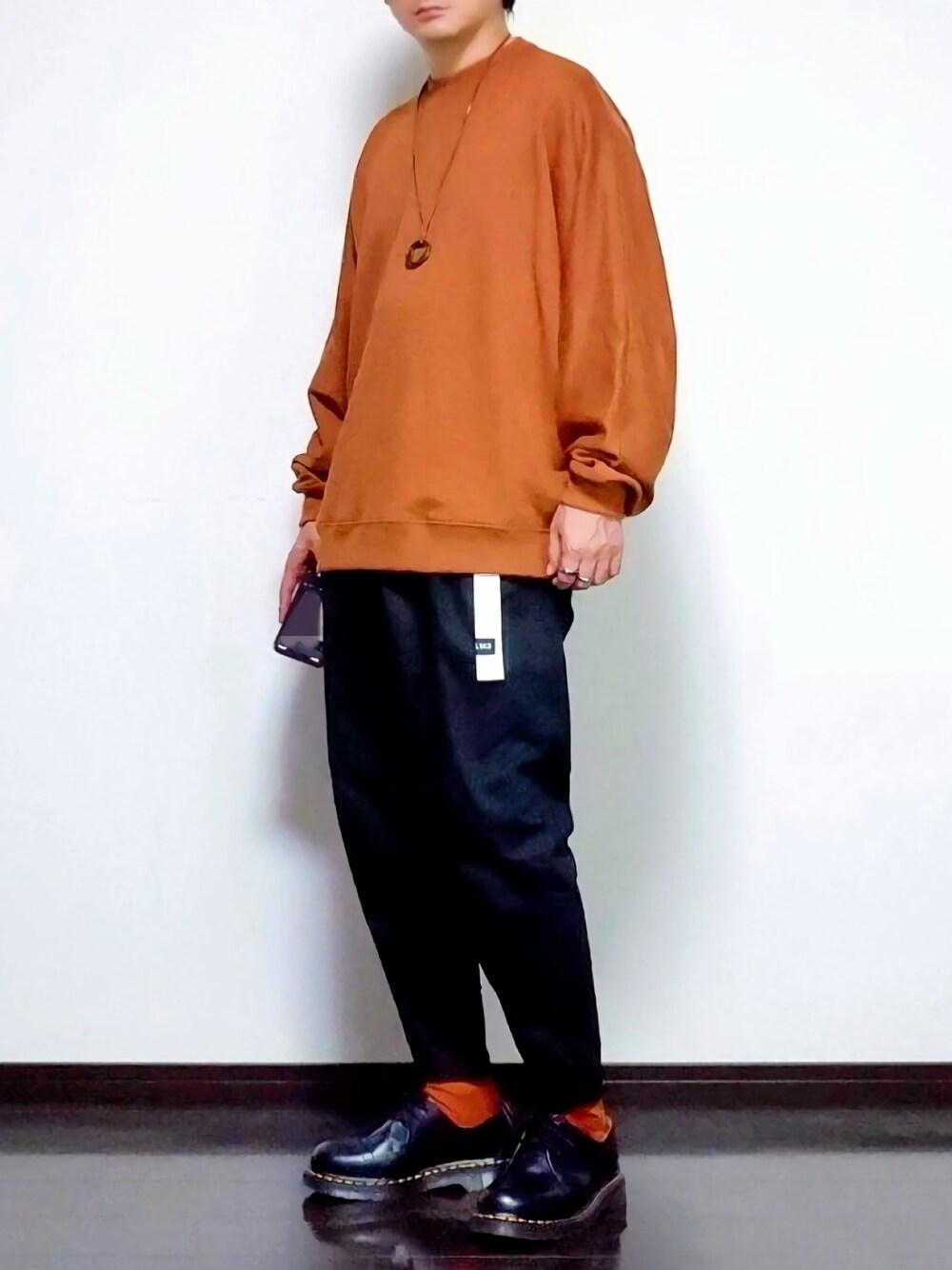 オレンジ系のスウェット、ブラック系のその他パンツ、ブラック系のブーツを着用したメンズの秋コーディネートの1枚目の写真