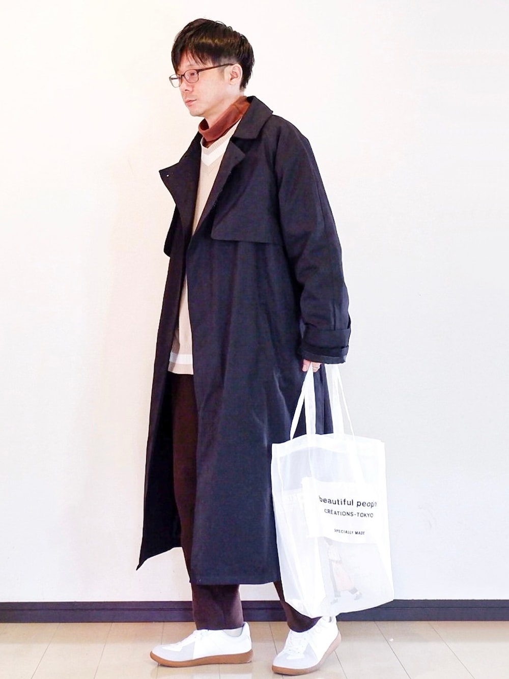 ブラック系のトレンチコート、ブラウン系のTシャツ/カットソー、ブラウン系のニット/セーターを着用したメンズの冬コーディネートの1枚目の写真