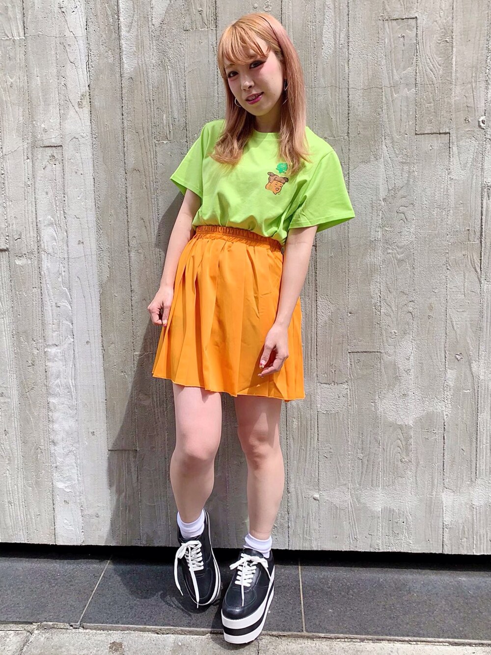 グリーン系のTシャツ/カットソー、オレンジ系のスカート、ブラック系のスニーカーを着用したレディースの夏コーディネートの1枚目の写真