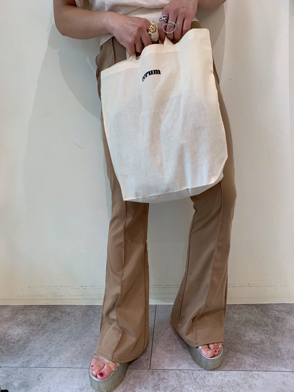 ベージュ系のトートバッグ、ベージュ系のパンツ、シルバー系のリングを着用したレディースの夏コーディネートの1枚目の写真