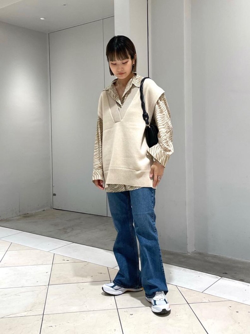 ブラック系のショルダーバッグ、ブルー系のデニムパンツ、ホワイト系のベストを着用したレディースの夏コーディネートの1枚目の写真