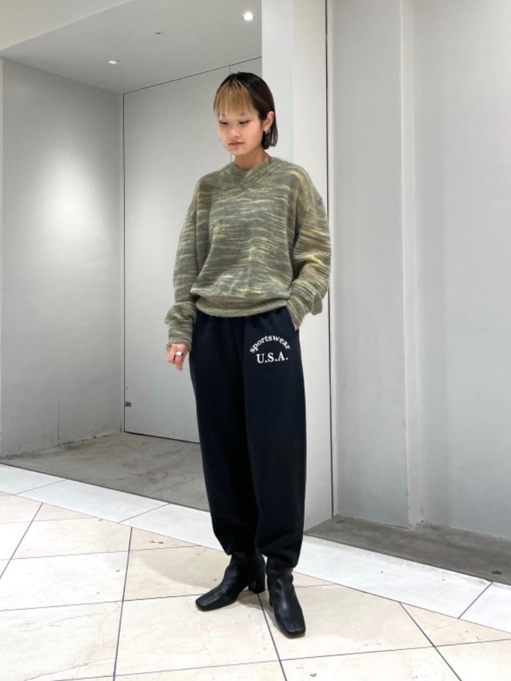 ブラック系のスウェットパンツ、ブラック系のブーツ、グリーン系のニット/セーターを着用したレディースの秋コーディネートの1枚目の写真