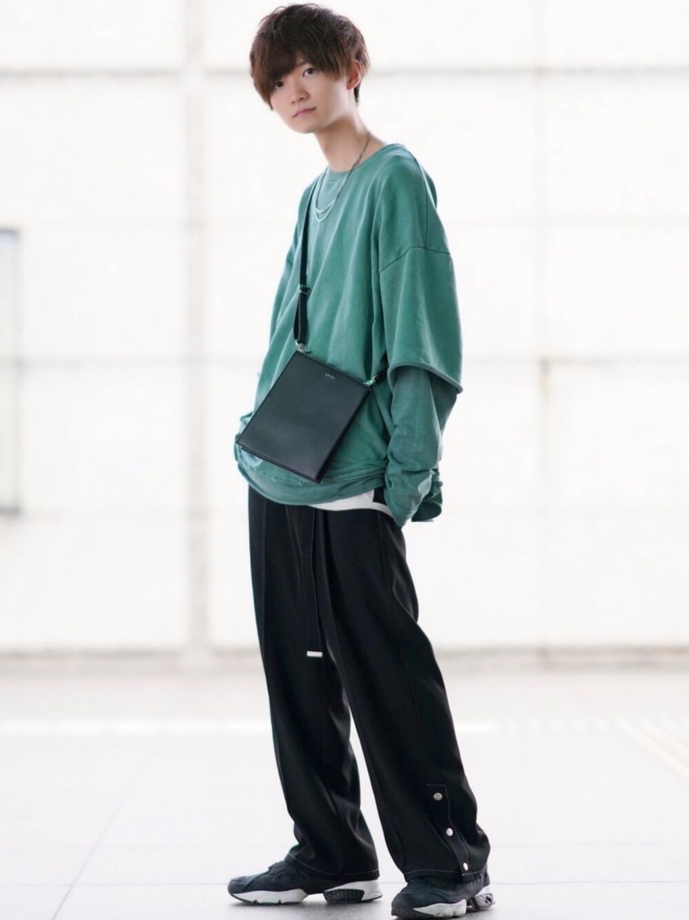 グリーン系のTシャツ/カットソー、ブラック系のショルダーバッグ、ブラック系のスニーカーを着用したメンズの春コーディネートの1枚目の写真