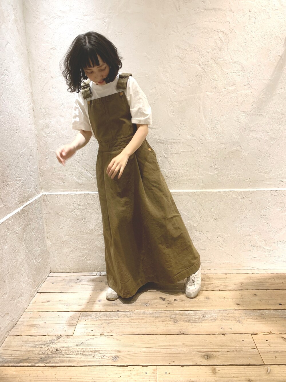 イエロー系のジャンパースカート、ホワイト系のTシャツ/カットソー、ホワイト系のスニーカーを着用したレディースの春コーディネートの1枚目の写真