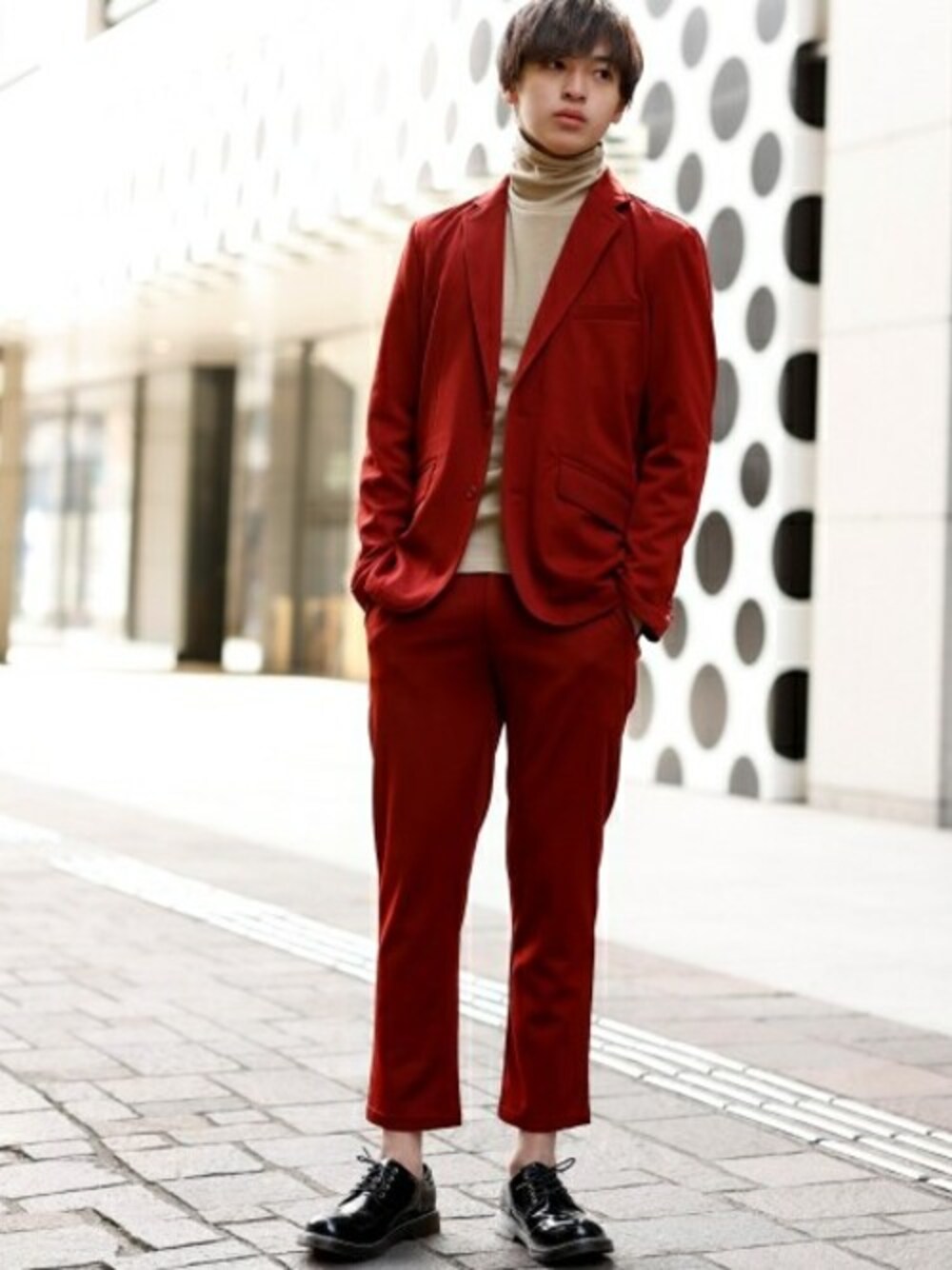 レッド系のテーラードジャケット、ベージュ系のTシャツ/カットソー、レッド系のスラックスを着用したメンズの冬コーディネートの1枚目の写真