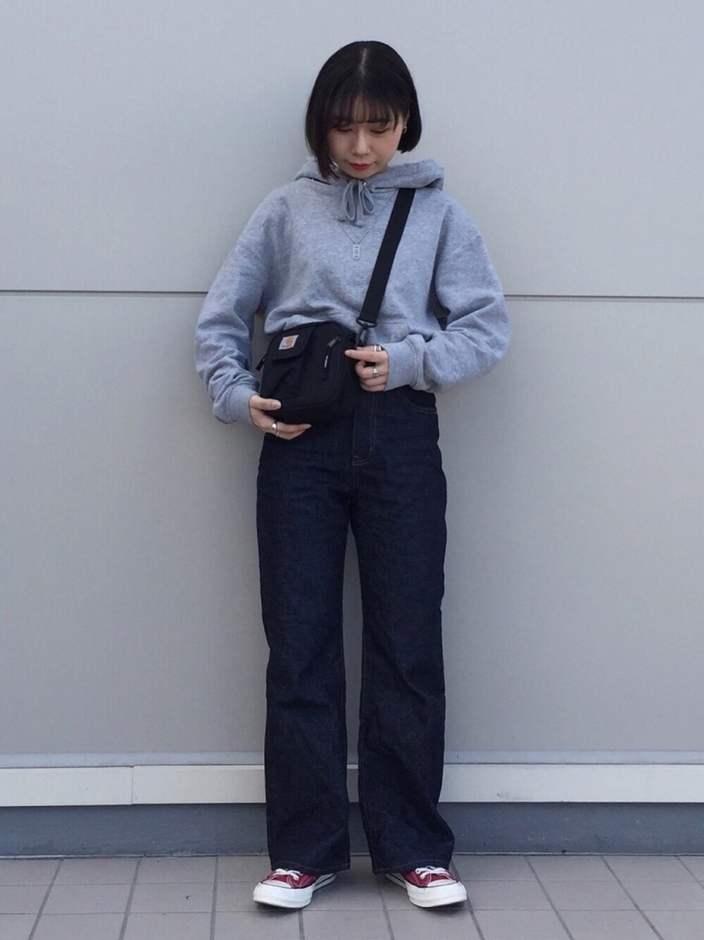 グレー系のパーカー、ブルー系のデニムパンツ、レッド系のスニーカーを着用したレディースの秋コーディネートの1枚目の写真