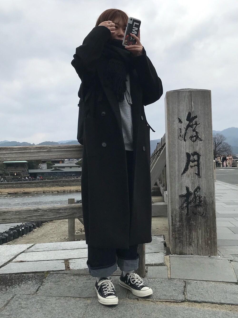 ブラック系のチェスターコート、ブルー系のデニムパンツ、ブラック系のスニーカーを着用したレディースの冬コーディネートの1枚目の写真