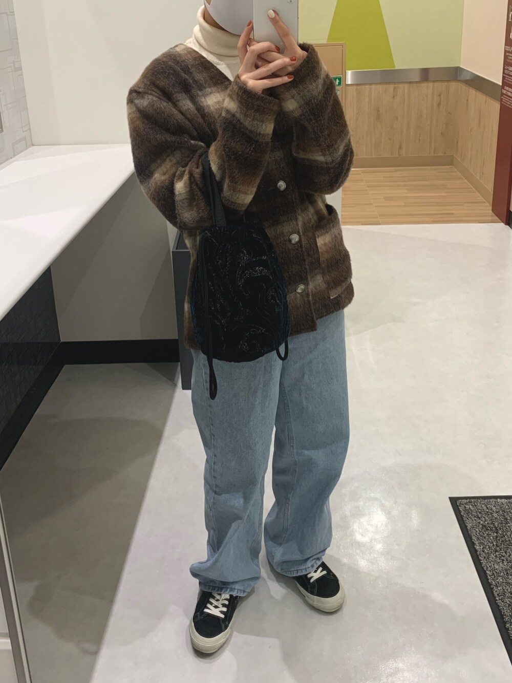 グリーン系のバッグ、ブラウン系のカーディガン/ボレロ、ブラック系のスニーカーを着用したレディースの冬コーディネートの1枚目の写真