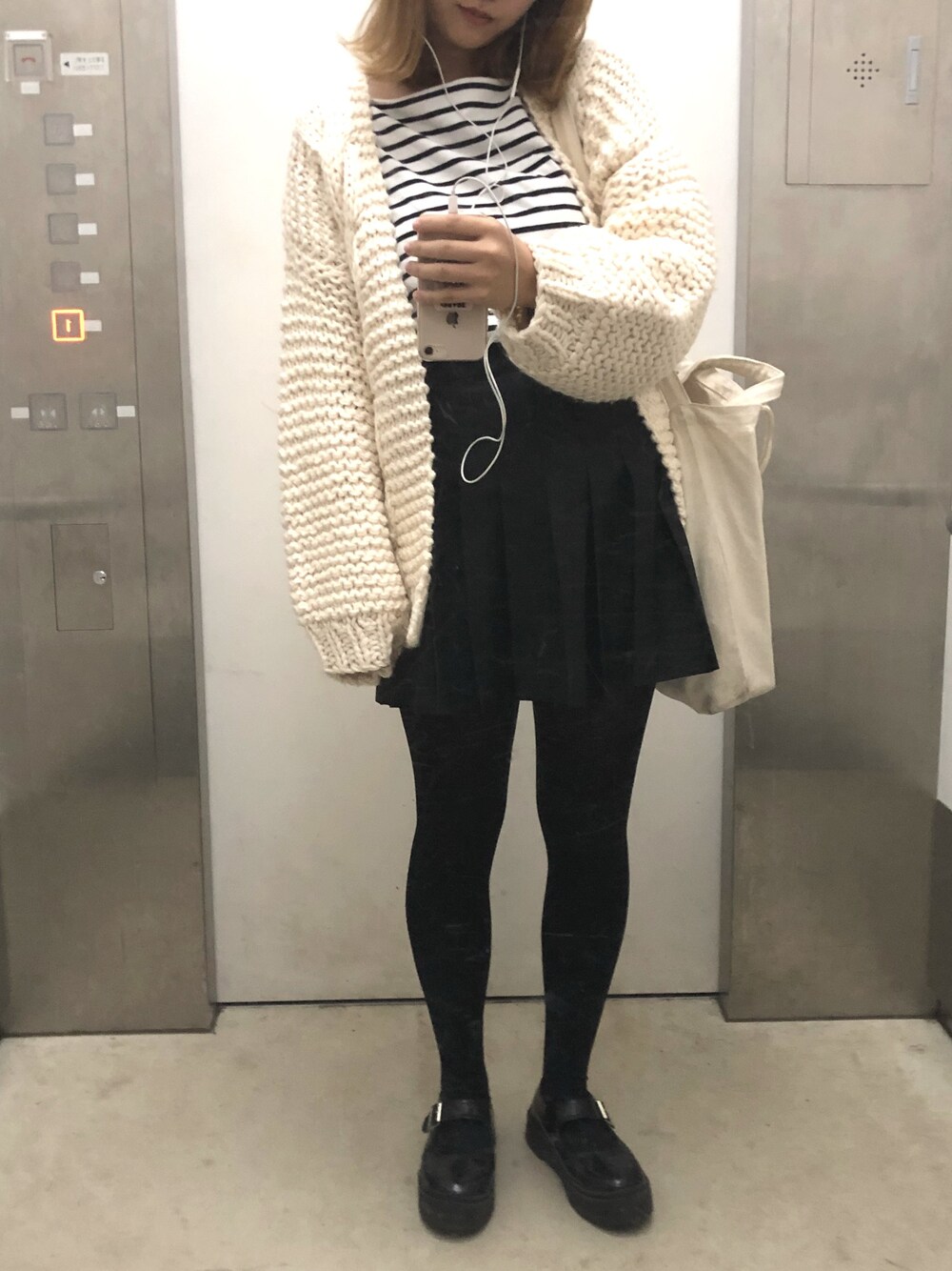 ホワイト系のカーディガン/ボレロ、ベージュ系のトートバッグ、ブラック系のスカートを着用したレディースの冬コーディネートの1枚目の写真