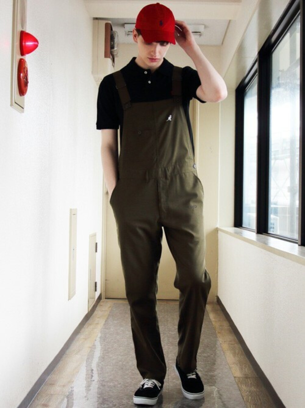 ブラック系のポロシャツ、グリーン系のサロペット/オーバーオール、レッド系のキャップを着用したメンズの夏コーディネートの1枚目の写真
