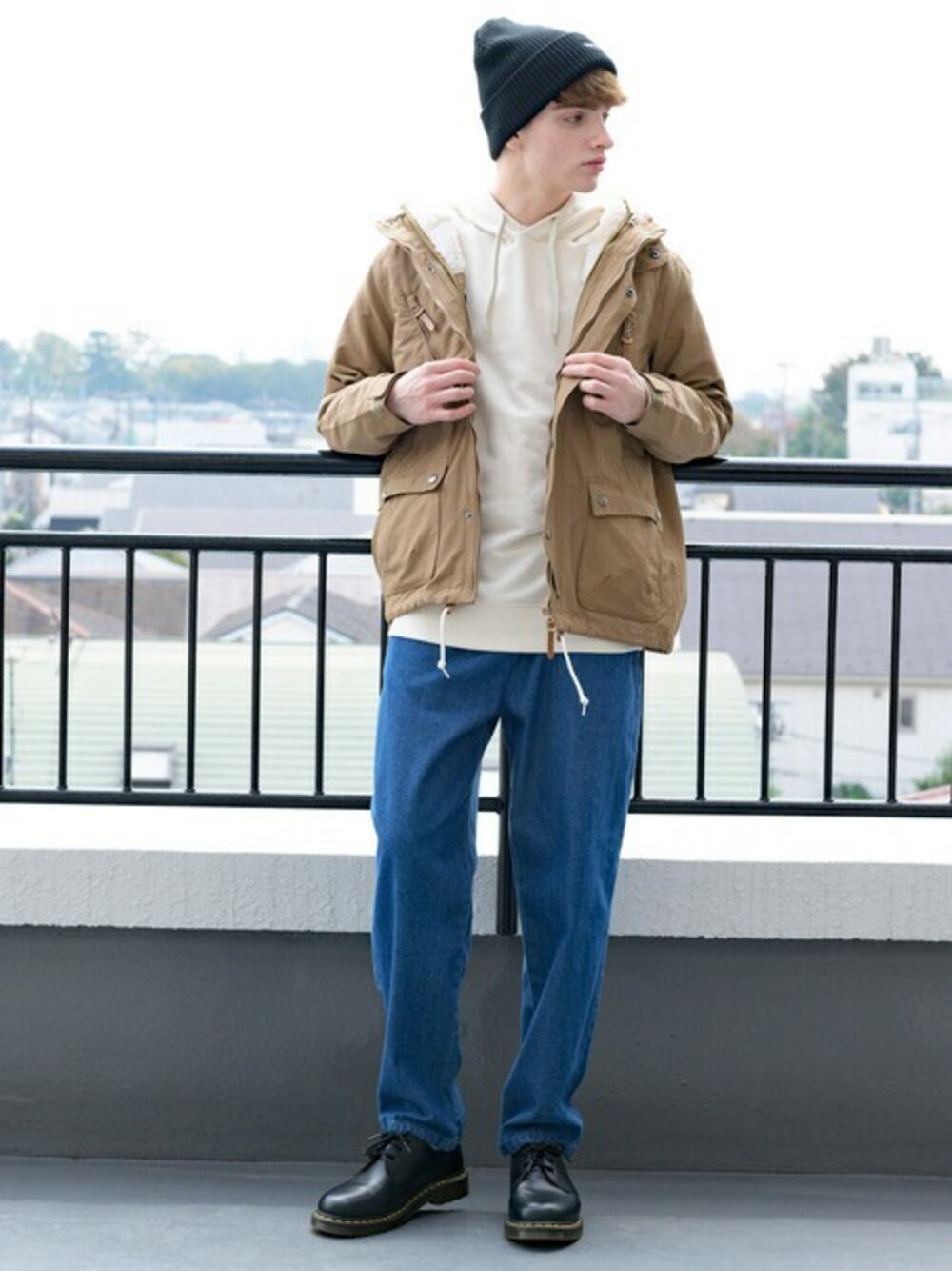 ベージュ系のマウンテンパーカー、ホワイト系のパーカー、ブルー系のデニムパンツを着用したメンズの冬コーディネートの1枚目の写真