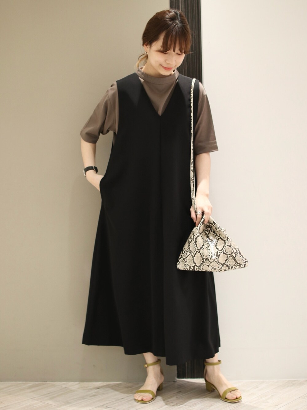 グリーン系のサンダル、ブラウン系のTシャツ/カットソー、ブラック系のジャンパースカートを着用したレディースの春コーディネートの1枚目の写真