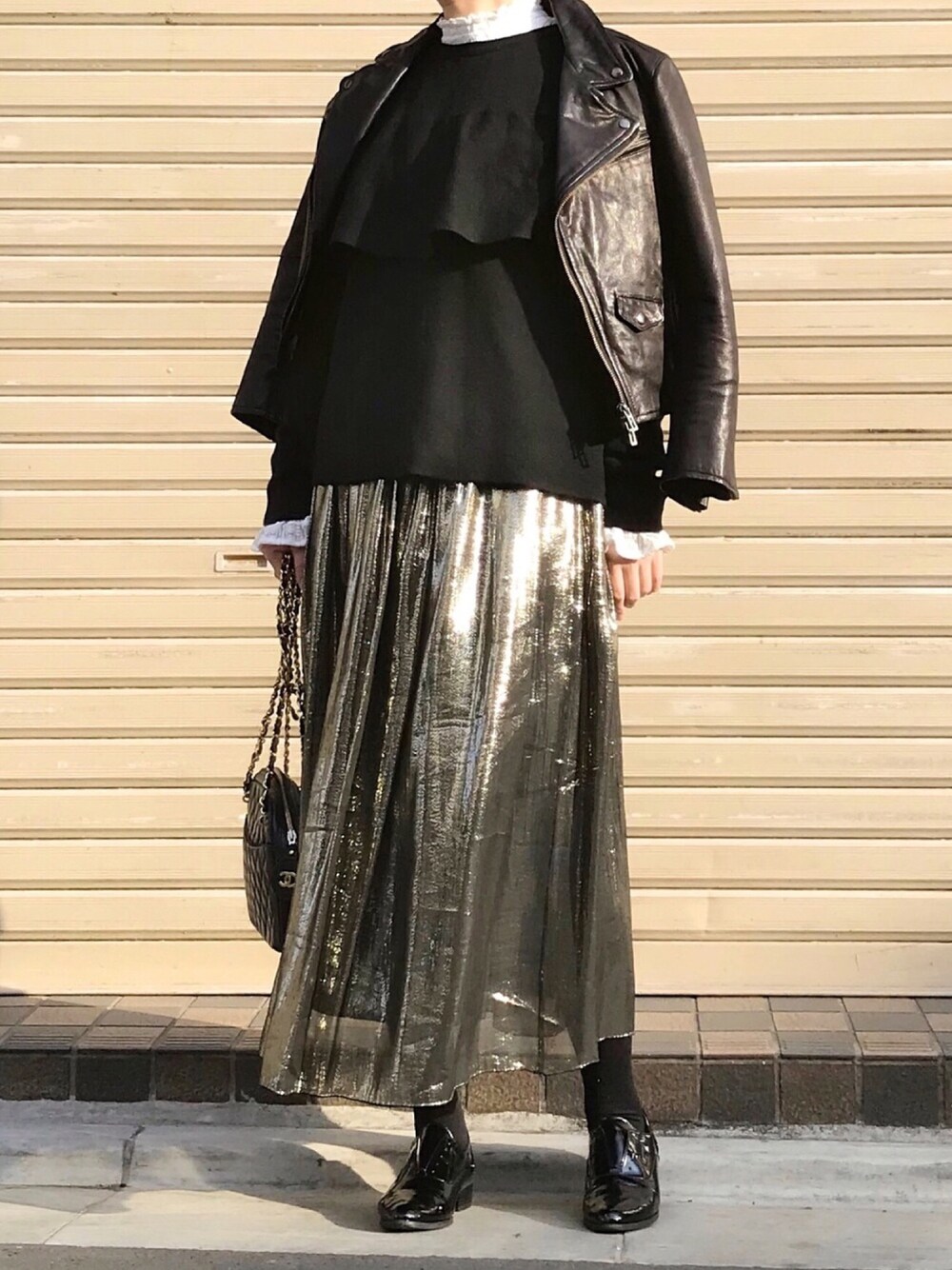 ブラック系のライダースジャケット、ゴールド系のスカート、ブラック系のパンプスを着用したレディースの冬コーディネートの1枚目の写真