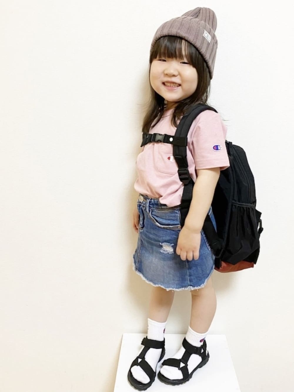 ピンク系のTシャツ/カットソー、ブラック系のバックパック/リュック、ブルー系のデニムスカートを着用したキッズの春コーディネートの1枚目の写真