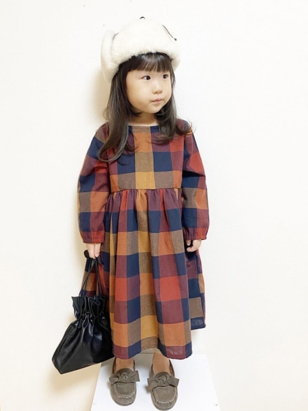 オレンジ系のワンピース、ブラック系のショルダーバッグ、ブラウン系のモカシン/デッキシューズを着用したキッズの秋コーディネートの1枚目の写真