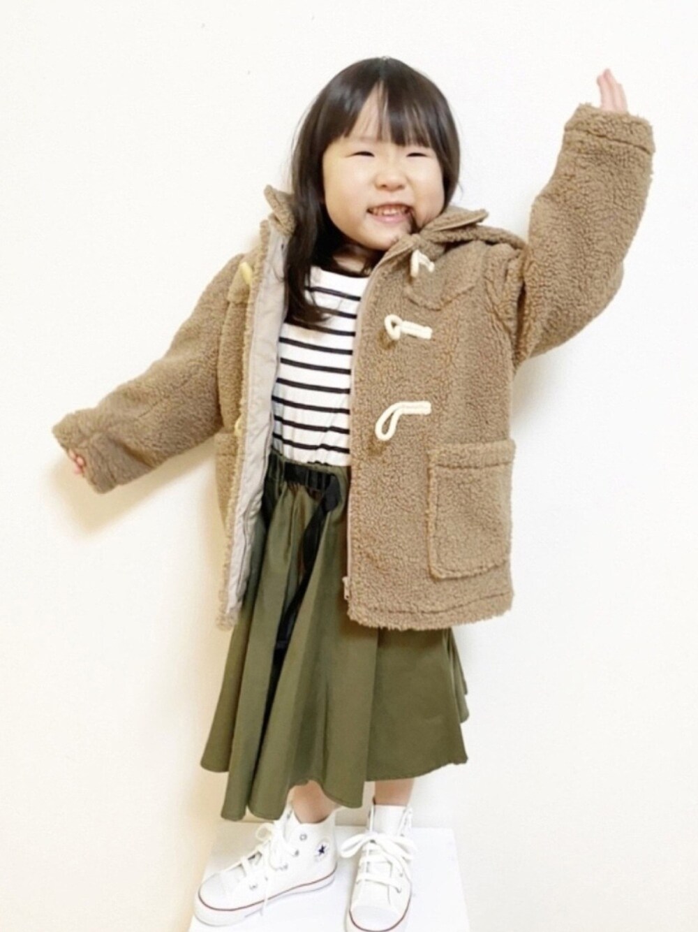 ブラウン系のダッフルコート、ブラック系のTシャツ/カットソー、ホワイト系のスニーカーを着用したキッズの冬コーディネートの1枚目の写真