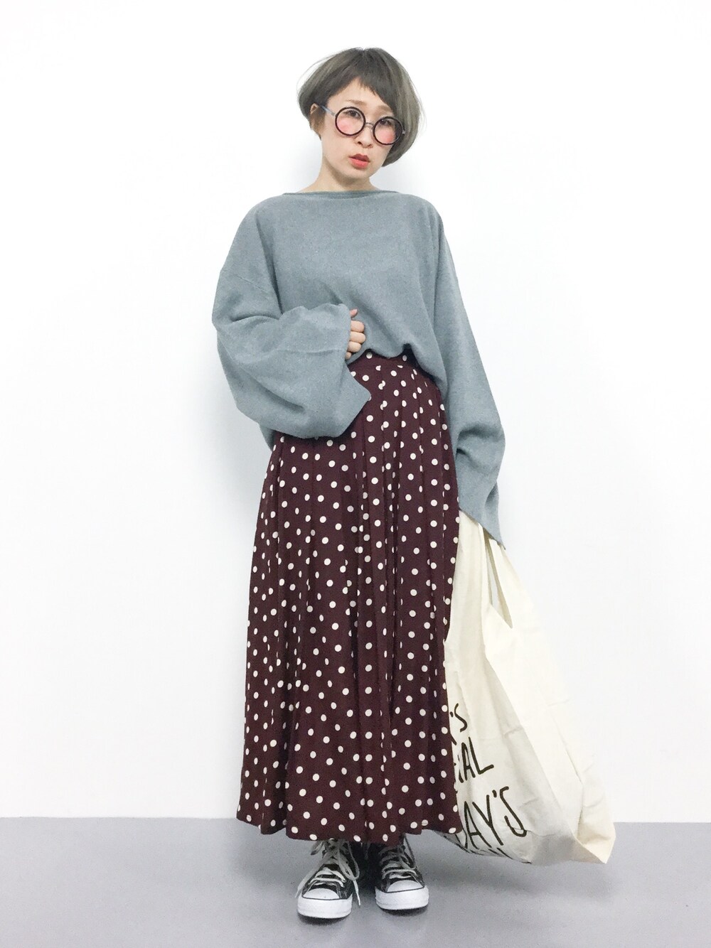 グレー系のニット/セーター、レッド系のスカート、ホワイト系のエコバッグ/サブバッグを着用したレディースの秋コーディネートの1枚目の写真