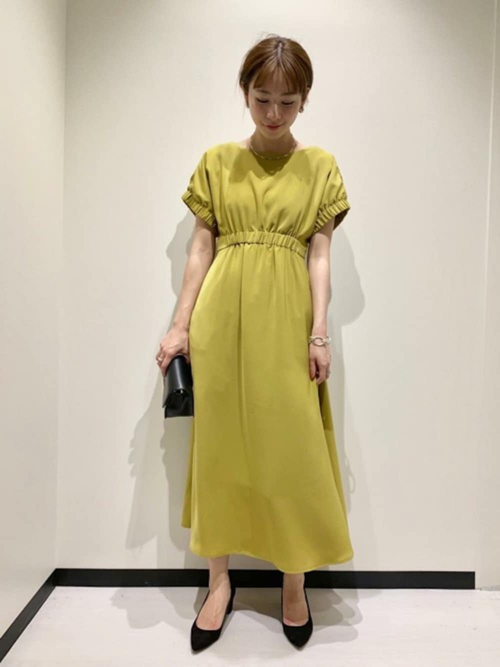 イエロー系のワンピース、ブラック系のパンプスを着用したレディースの春コーディネートの1枚目の写真