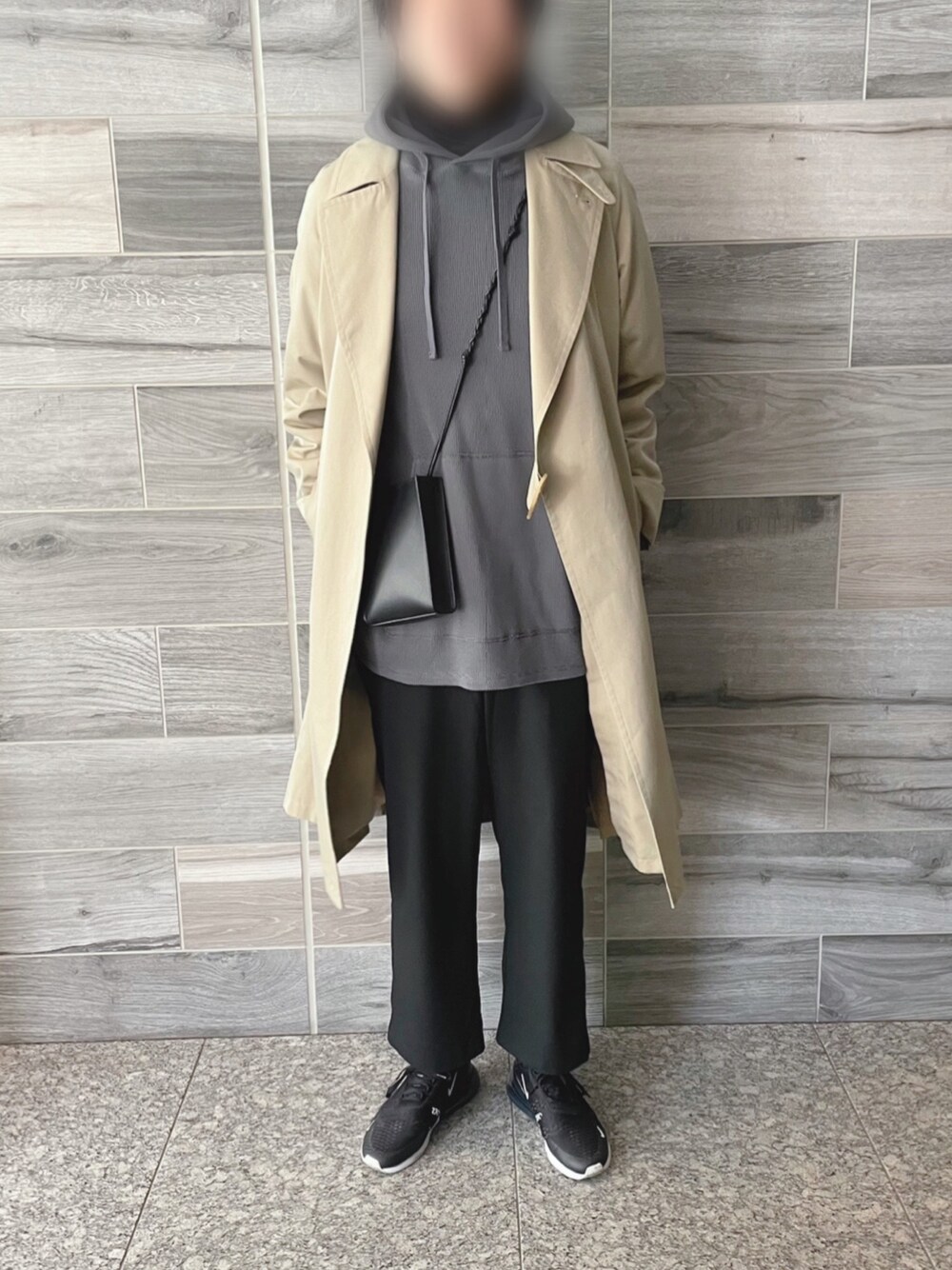 ベージュ系のトレンチコート、グレー系のパーカー、ブラック系のショルダーバッグを着用したメンズの冬コーディネートの1枚目の写真