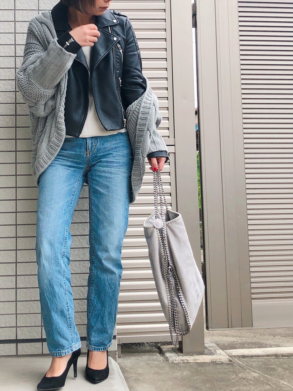 ブラック系のライダースジャケット、グレー系のニット/セーター、ブルー系のデニムパンツを着用したレディースの冬コーディネートの1枚目の写真
