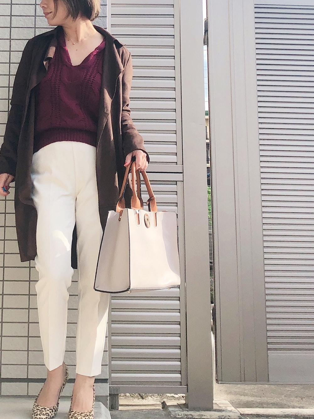 ブラウン系のトレンチコート、ブラウン系のニット/セーター、ホワイト系のパンツを着用したレディースの冬コーディネートの1枚目の写真