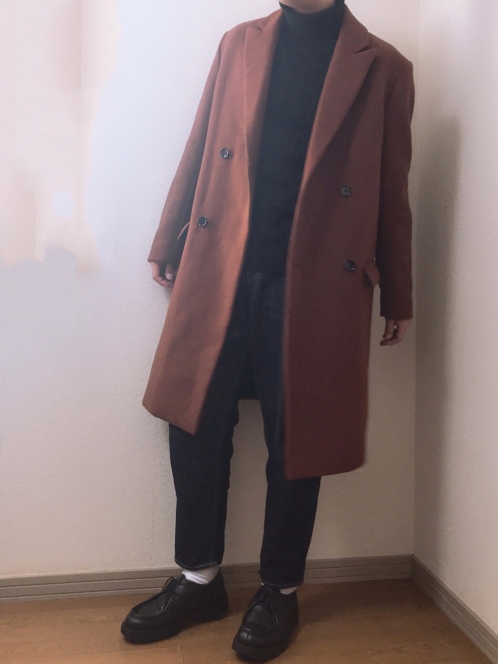 ブラウン系のチェスターコート、ブラック系のニット/セーター、ブルー系のデニムパンツを着用したメンズの冬コーディネートの1枚目の写真