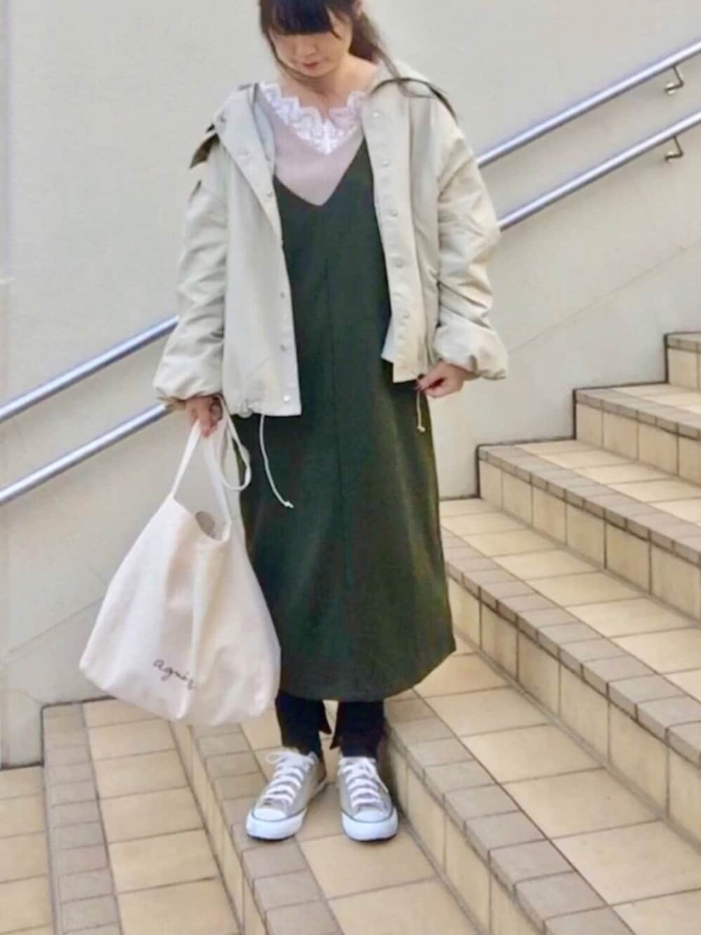 ベージュ系のナイロンジャケット、ベージュ系のTシャツ/カットソー、グリーン系のジャンパースカートを着用したレディースの秋コーディネートの1枚目の写真