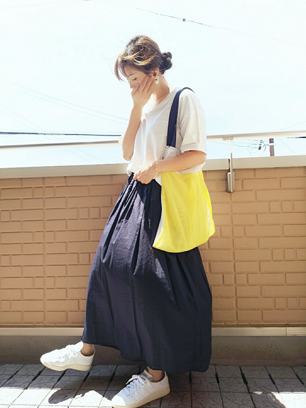 イエロー系のトートバッグ、ホワイト系のスニーカー、ブルー系のスカートを着用したレディースの夏コーディネートの1枚目の写真