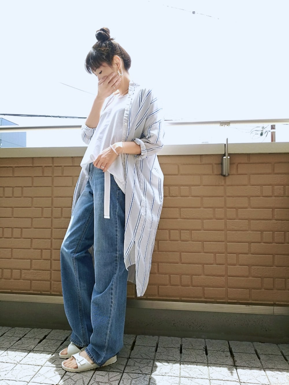 グレー系のワンピース、ブルー系のデニムパンツ、ホワイト系のサンダルを着用したレディースの夏コーディネートの1枚目の写真