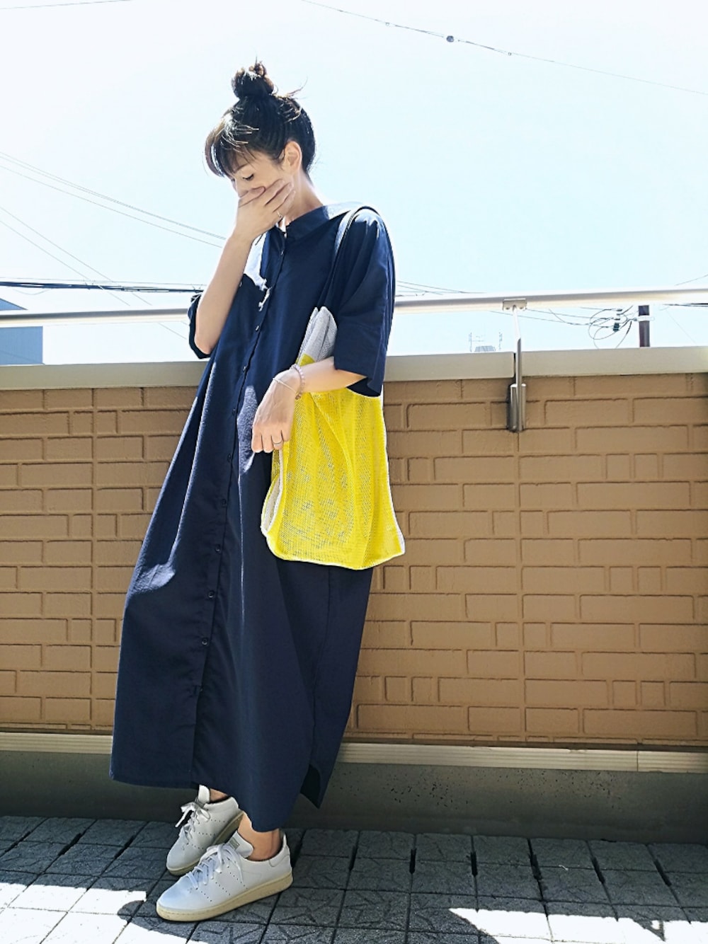 ブルー系のシャツワンピース、ホワイト系のスニーカー、イエロー系のトートバッグを着用したレディースの夏コーディネートの1枚目の写真