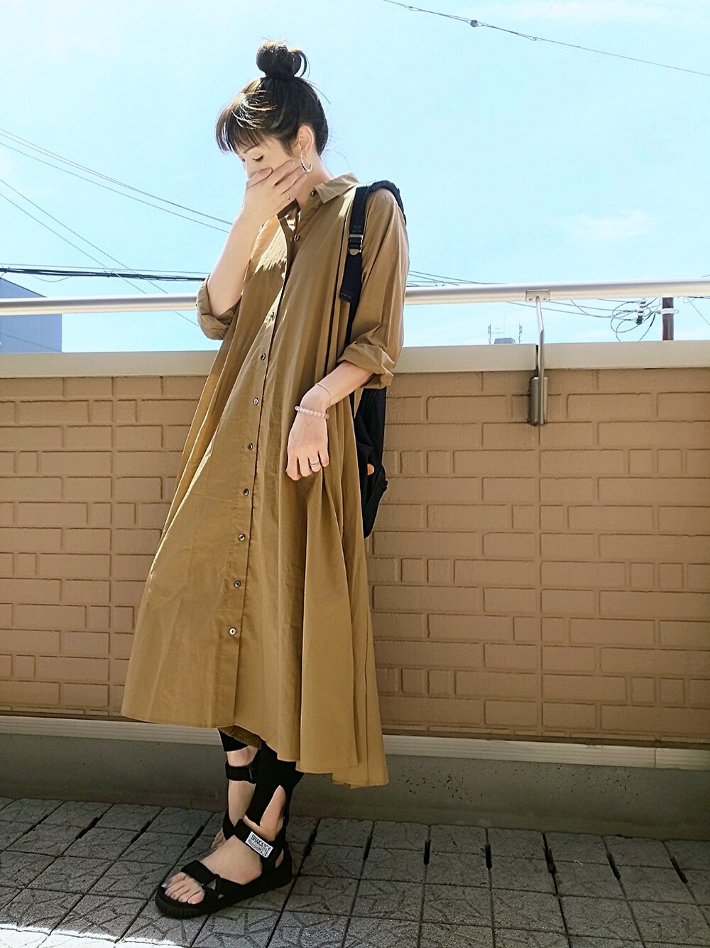 ブラック系のバックパック/リュック、イエロー系のシャツワンピース、ブラック系のサンダルを着用したレディースの夏コーディネートの1枚目の写真