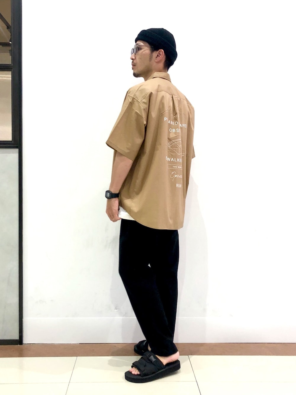 ブラック系のスラックス、ベージュ系のシャツ/ブラウス、ブラック系のサンダルを着用したメンズの夏コーディネートの1枚目の写真