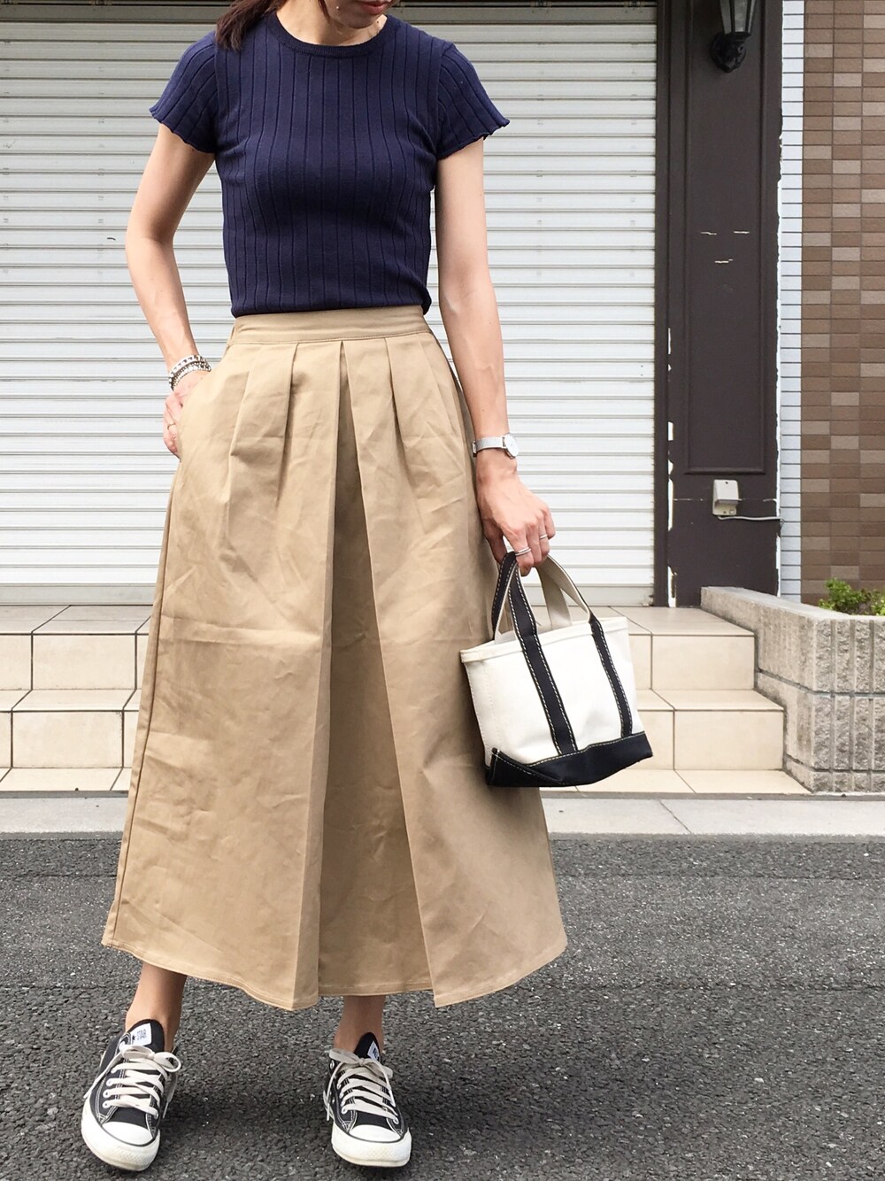 ベージュ系のスカート、ホワイト系のトートバッグ、ブラック系のスニーカーを着用したレディースの夏コーディネートの1枚目の写真