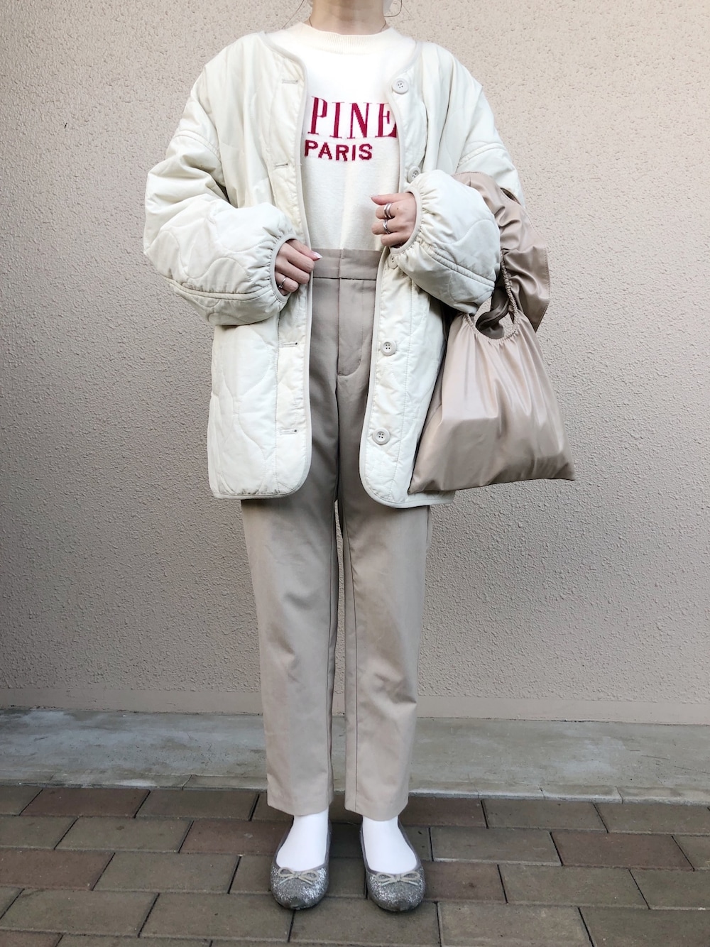 ホワイト系のブルゾン、ベージュ系のパンツ、ベージュ系のハンドバッグを着用したレディースの冬コーディネートの1枚目の写真