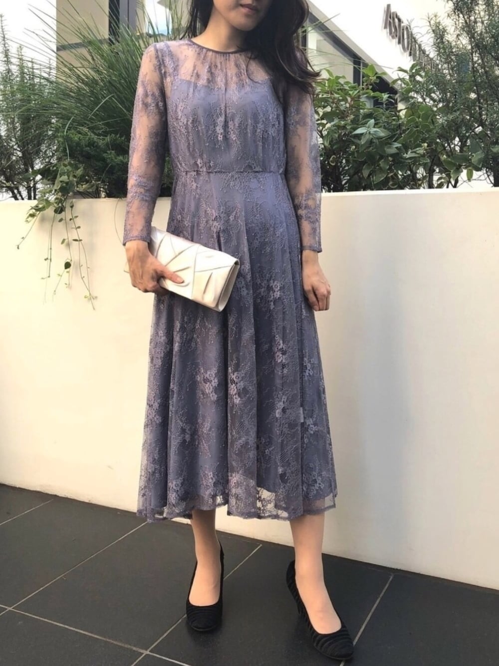 パープル系のドレス、ホワイト系のクラッチバッグ、ブラック系のパンプスを着用したレディースの秋コーディネートの1枚目の写真