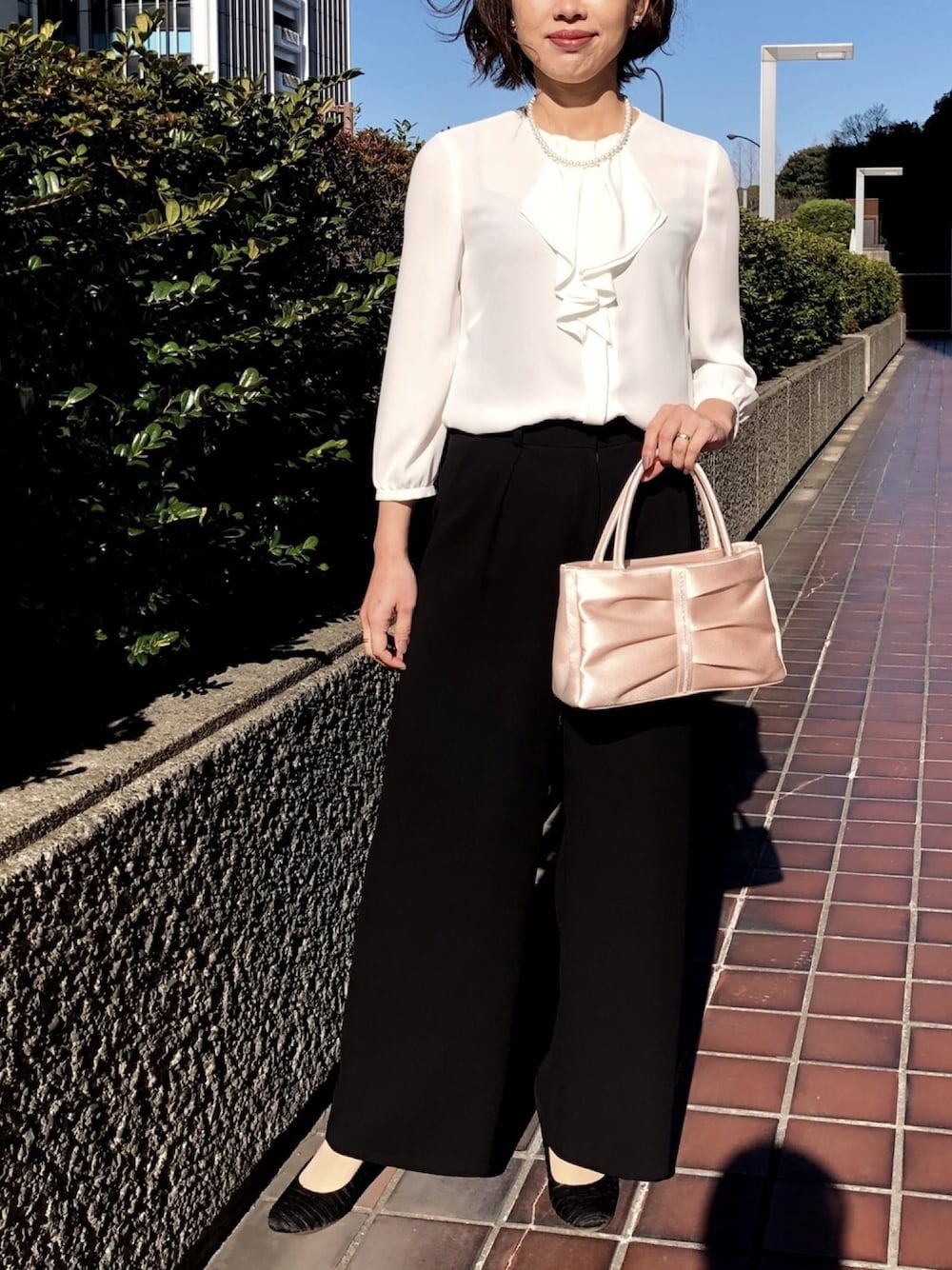 ブラック系のスーツセット、ブラック系のパンプス、ベージュ系のハンドバッグを着用したレディースの冬コーディネートの1枚目の写真