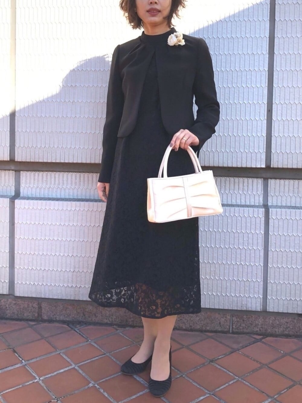 ブラック系のスーツセット、ベージュ系のハンドバッグ、ブラック系のパンプスを着用したレディースの冬コーディネートの1枚目の写真